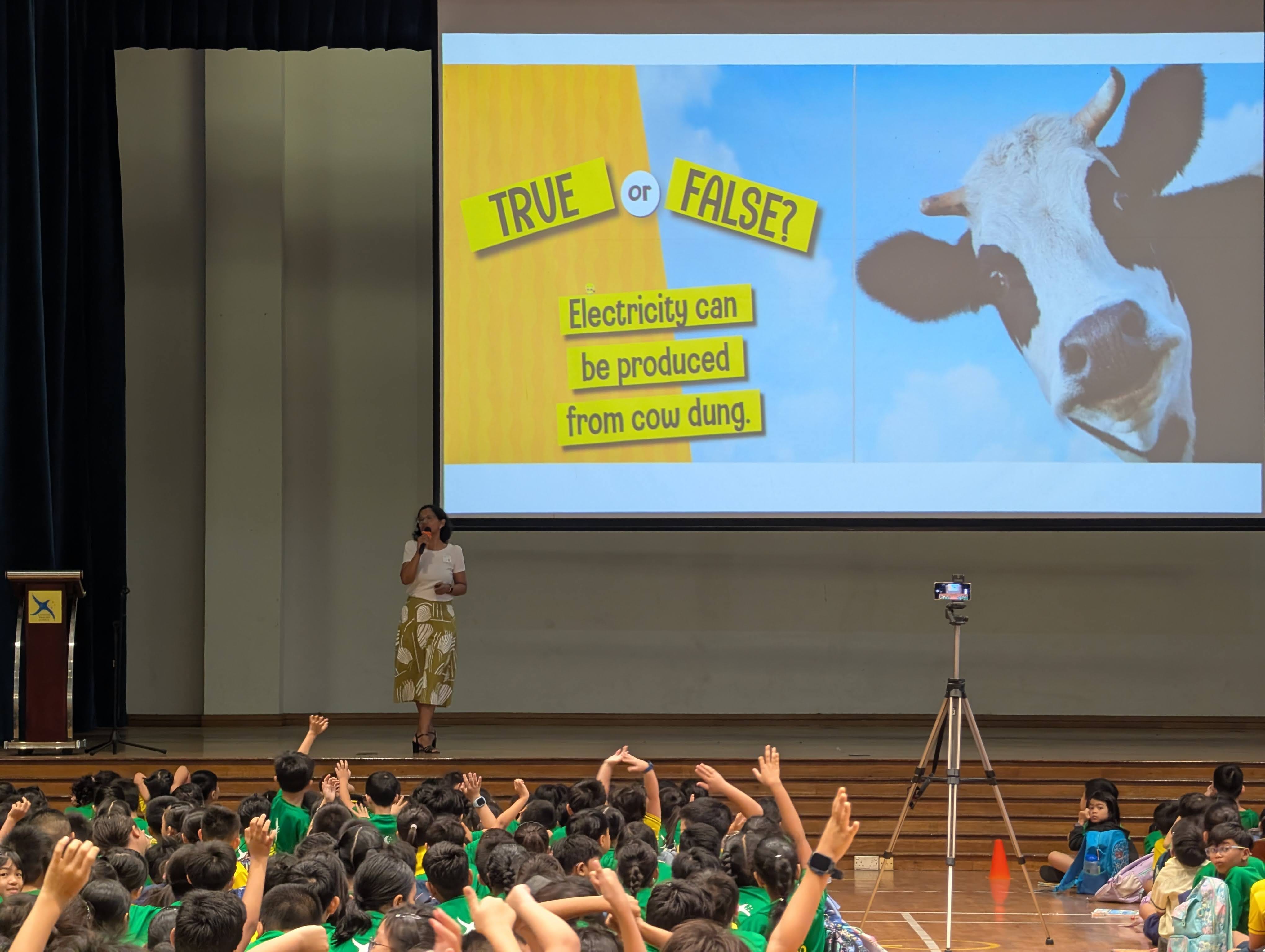 Ms Manisha Nayak on stage with her presentation slide on a "True or False?" slide about whether electricity can be produced from cow dung